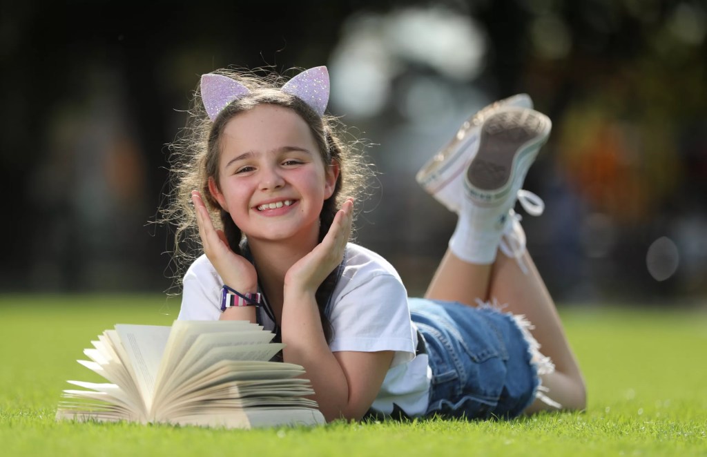 Girl wearing cat ears, relaxing on the grass with a book. Image for the Good Friday Appeals Cardiology Research by Alex Coppel