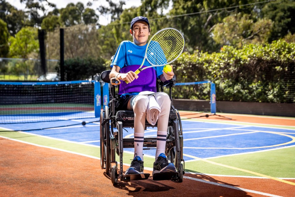 Patient in a wheelchair holding a tennis racquet, on a tennis court.